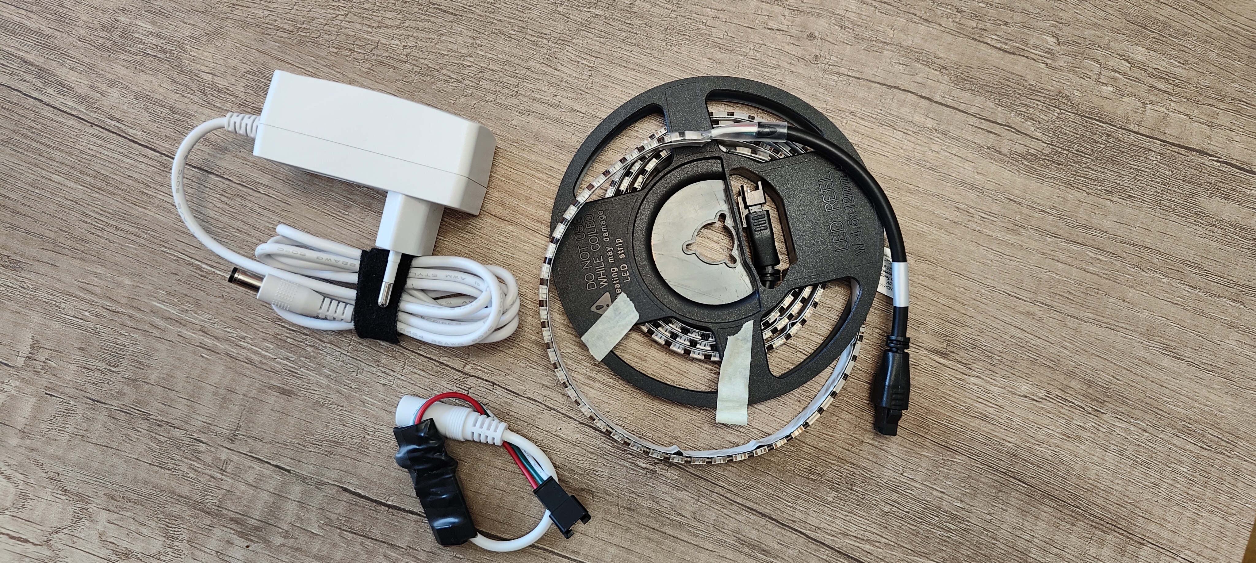 The first DreamScaler set on a wooden work surface: a coiled RGBW LED strip, white power adapter, and wired controller assembly.